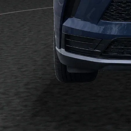 Close-up of the SUV’s front corner and tyre on the studio’s dark carpet, seen from the front, with the contact shadow under it.