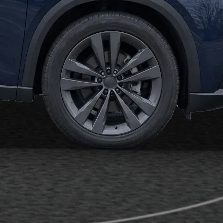 Close-up of the SUV’s front wheel on the studio’s dark carpet, seen from the side, with the contact shadow under the tyre.