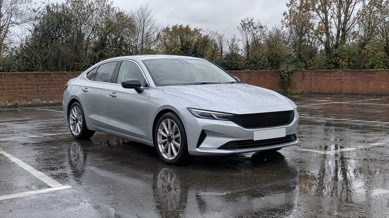 A fictional silver saloon on a rain-soaked car lot, mirrored in a puddle, front three-quarter view; a sample photo made with TunePixel AI.