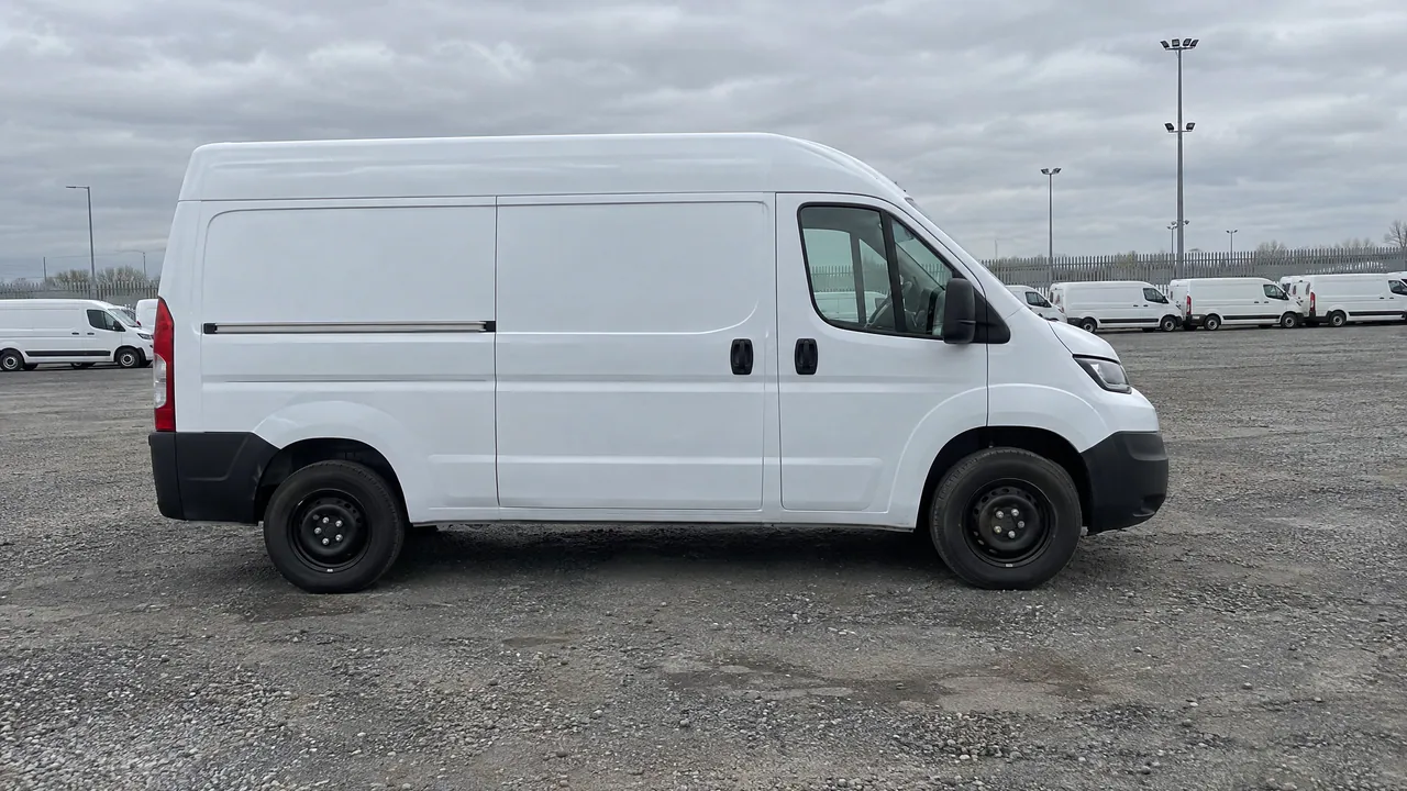 A fictional white panel van in an auction yard with a line of other vans far behind it, side view; a sample photo made with TunePixel AI.